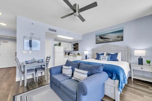 A modern bedroom with a bed, a blue sofa, a dining table, and a kitchen area.