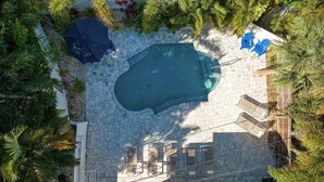 An aerial view of a swimming pool surrounded by a tiled patio, with lounge chairs and umbrellas.