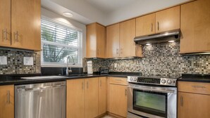 A modern kitchen with wooden cabinets, a stainless steel dishwasher, a double oven, and a tiled backsplash.