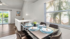 A dining area with a long table set for six, white plates, blue placemats, and a small potted plant.