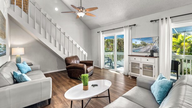 A spacious living room with a staircase, a ceiling fan, and a view of the outdoors.