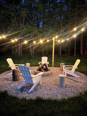 Un espace de détente circulaire avec des fauteuils Adirondack, un foyer et des guirlandes lumineuses.