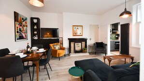 Ein modernes Wohnzimmer mit Essbereich, Kamin und einer durchgehenden Tür sichtbaren Küche.