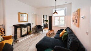 Ein Wohnzimmer mit Kamin, einer schwarzen Couch, einem gelben Sessel und einem Essbereich mit Tisch und Stühlen.