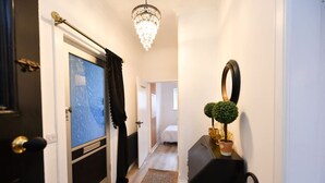 Ein Flur mit einer Chandelüster, einer Tür mit Fenster, einem Bett im Hintergrund und einer kleinen Pflanze auf einem Tisch.