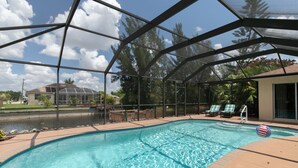 A swimming pool with a glass enclosure, lounge chairs, and a view of a house and trees. - Cape Coral Serenity Waterfront Walking Distance to Shopping & Restaurants (Cape Coral)