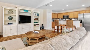 A modern living room with a large sofa, a television, and built-in shelving. - Cape Coral Serenity Waterfront Walking Distance to Shopping & Restaurants (Cape Coral)