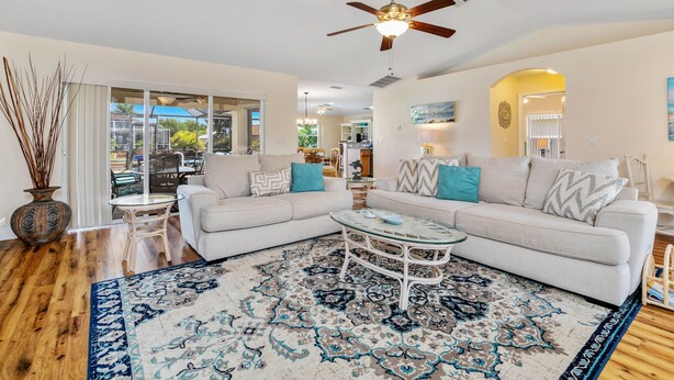 A living room with a large window, a ceiling fan, a coffee table, and a patterned rug. - Cape Coral Serenity Waterfront Walking Distance to Shopping & Restaurants (Cape Coral)