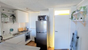 Una cocina compacta con armarios blancos, un refrigerador de acero inoxidable, un microondas, una estufa a gas y un fregadero.