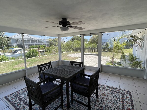 Un patio techado con mesa y sillas, ventanas amplias y un ventilador de techo.