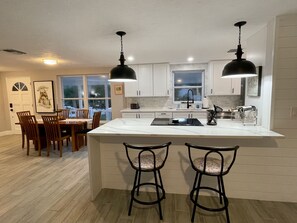 A modern kitchen with white cabinets, a large island, two bar stools, and pendant lighting.
