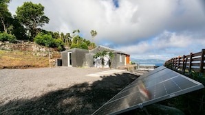 A solar panel installation in a rural setting with a small building and a wooden fence. - Adegada Quinta- Beautiful Cottage in Madalena (Madalena - Pico)