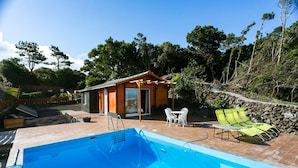 A swimming pool with a wooden deck, a small wooden building with a glass door, and green lounge chairs. - Adegada Quinta- Beautiful Cottage in Madalena (Madalena - Pico)