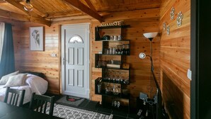 A cozy wooden cabin room with a bed, a desk, and shelves with glassware. - Adegada Quinta- Beautiful Cottage in Madalena (Madalena - Pico)