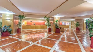 Un hall d’entrée spacieux, doté d’un comptoir de réception, de plantes en pot et d’un sol carrelé.