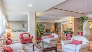 Un hall d’entrée spacieux au design moderne, aménagé avec différents types de sièges, notamment des canapés et des fauteuils, une table basse centrale et des plantes en pot.