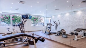Une salle de sport équipée de machines de cardio, d’appareils de musculation et de grandes fenêtres offrant une vue sur la verdure.
