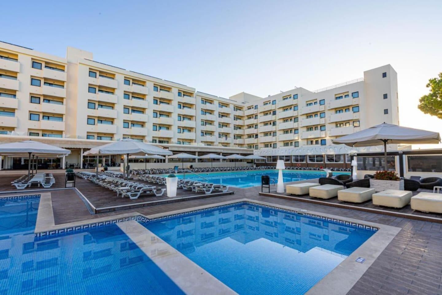 Hotel med swimmingpool, liggestole og udendørs siddeområder.