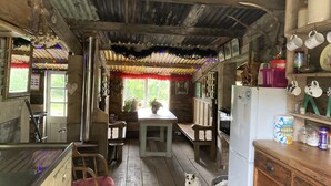 Ett rustikt kök med träväggar och ett tak av korrugerad plåt, inrett med ett kylskåp, trästolar, ett bord och en hund.