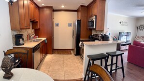 A compact kitchen with wooden cabinets, a refrigerator, a microwave, and a coffee maker. There is a dining area with a table and chairs. - C2 Pet-friendly, 1 BR, 1 BA, sleeps 5 (St. Simons Island)