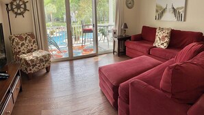 A living room with a red sofa, a patterned armchair, a TV stand, and a view through a glass door to an outdoor area with a table and chairs. - C2 Pet-friendly, 1 BR, 1 BA, sleeps 5 (St. Simons Island)