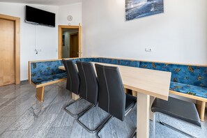 Uma sala de conferências com uma mesa comprida, quatro cadeiras, um banco, uma televisão e um relógio na parede.