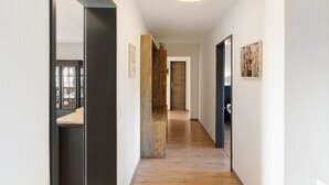 A hallway with wooden flooring, a black-framed door, and a ceiling light fixture.