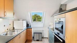 A compact kitchen with a window, stainless steel appliances, and wooden cabinets.
