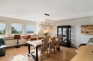 Un coin repas avec une table et des chaises en bois, un buffet noir aux portes vitrées et une vue dégagée grâce à de grandes fenêtres.