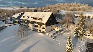 A multi-story building with a sloped roof, surrounded by snow-covered trees and a clear sky.