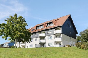 Un immeuble résidentiel à plusieurs étages, doté d’un toit en pente, de balcons et d’une pelouse devant.