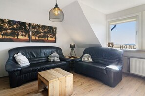 Un salon moderne avec un canapé en cuir noir, une table basse en bois et une grande fenêtre offrant une belle vue.