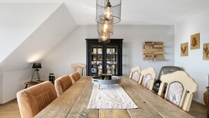 A dining area with a long wooden table, upholstered chairs, a black cabinet with glass doors, and a hanging light fixture.