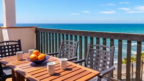 Ein Holztisch mit einer Schüssel Orangen und zwei weißen Tassen, mit Blick auf das türkisfarbene Meer.
