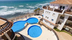 Ein Poolbereich mit zwei runden Pools, Blick auf den Strand und einem Gebäude mit Balkonen.