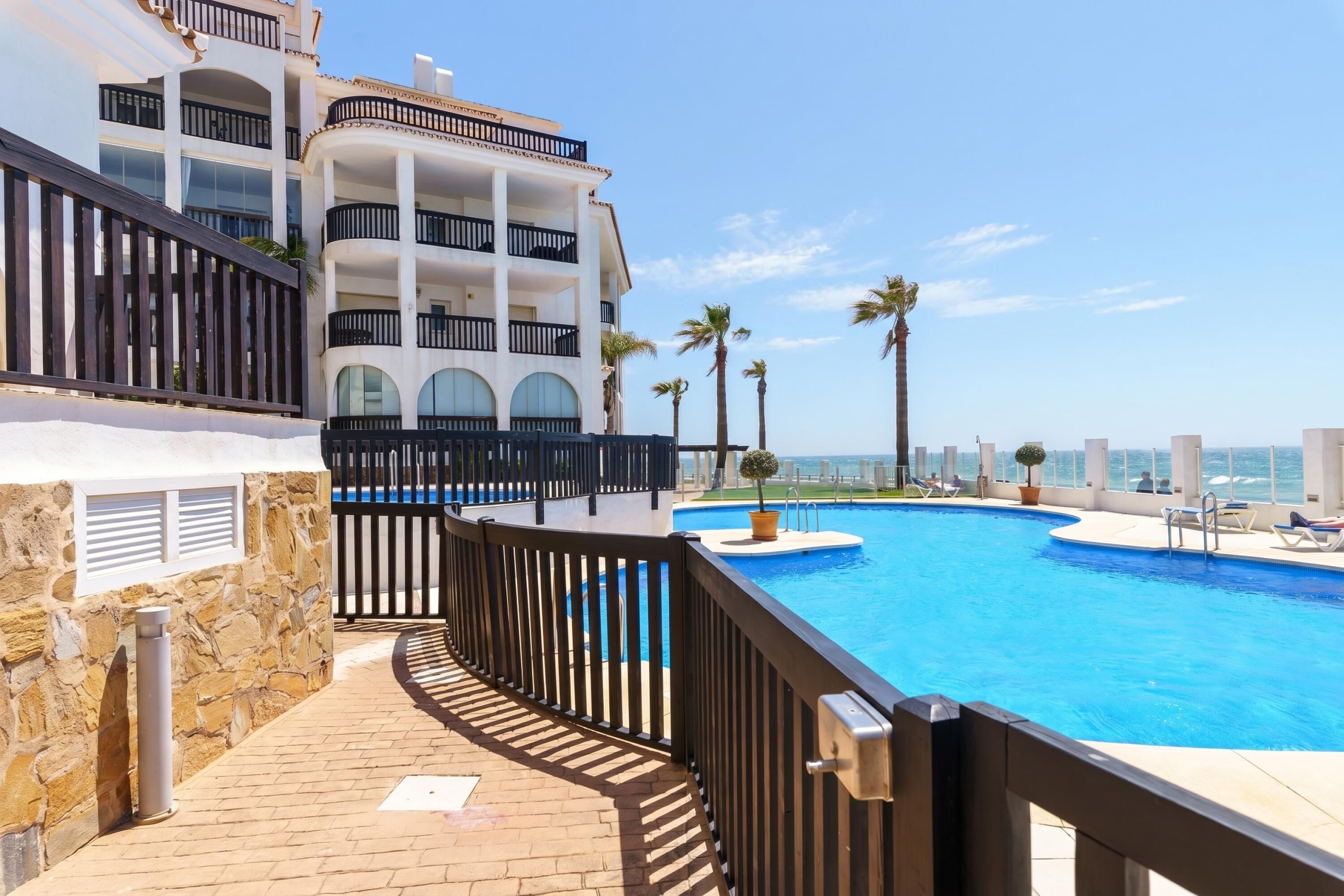 A swimming pool with a stone wall and a balcony with black railings.