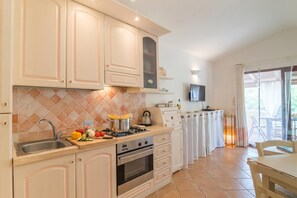 Una cocina con lavamanos, estufa y encimera con alimentos. Hay un televisor montado en la pared y una ventana con cortinas.