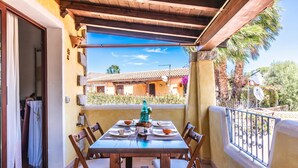 A balcony with a wooden table set for dining, a view of a building with a tiled roof, and a palm tree. - Dimora di Rosy Pittulongu, Pittulongu, Italy (Pittulongu)