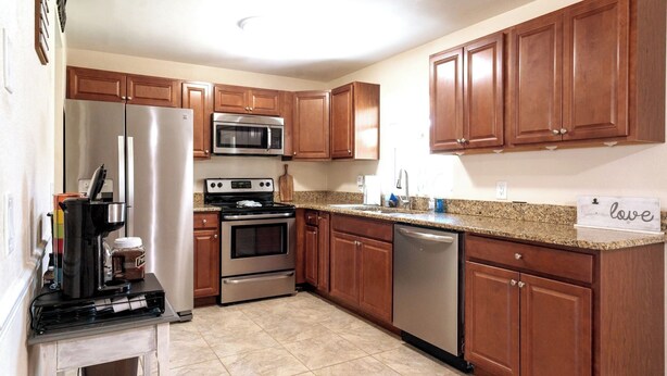 A kitchen with wooden cabinets, stainless steel appliances, and a granite countertop. - Space Coast Retreat: Games, Hot Tub, Fenced yard, Pool Table + Massage Chair (Cocoa)