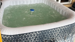 An inflatable hot tub with a blue handle, a white border, and a geometric pattern on the sides. It is placed against a brick wall with a sliding glass door in the background. - Space Coast Retreat: Games, Hot Tub, Fenced yard, Pool Table + Massage Chair (Cocoa)