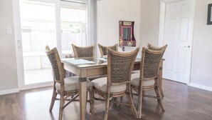 A dining area with a glass-top table surrounded by four wicker chairs. - Space Coast Retreat: Games, Hot Tub, Fenced yard, Pool Table + Massage Chair (Cocoa)