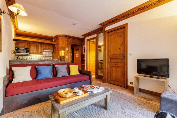 Een gezellige woonkamer met een rode bank, houten kasten, een televisie en een keuken op de achtergrond.