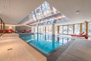 Ein Innenpool mit klarer Glasdecke, roten Liegestühlen und großen Fenstern.