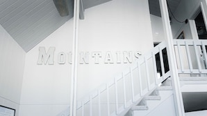 A staircase with a railing and a clock on the wall. The word "MOUNTAINS" is displayed above the stairs. - The Little Red Barn w/ Spectacular Views & Less than 1 mile - Blue Ridge Parkway (Hillsville)