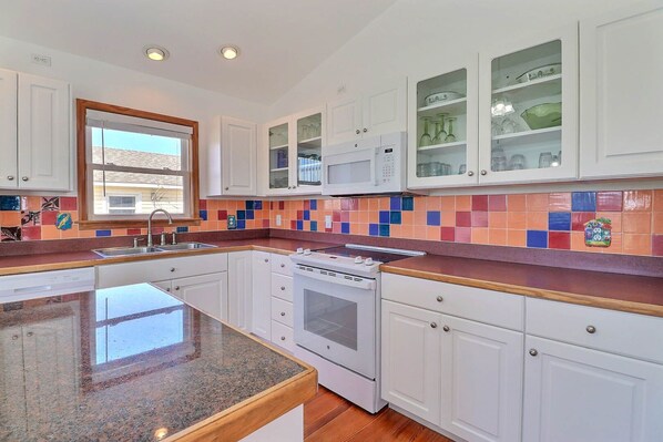 A modern kitchen with white cabinets, a granite countertop, a built-in oven, and a colorful backsplash. - 5167 Wings As Eagles * 5 Min Walk to Beach (Kill Devil Hills)