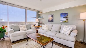 A living room with two light-colored sofas, a coffee table, a floor lamp, and a large window.
