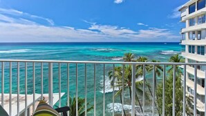 A balcony with a view of the ocean and a building with multiple floors.