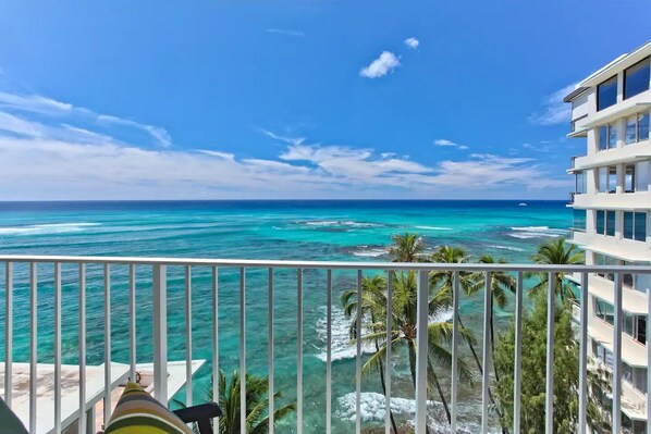 A balcony with a view of the ocean and a building with multiple floors.