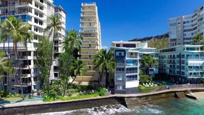A coastal hotel with multiple high-rise buildings, palm trees, and a clear view of the ocean.