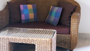 A wicker sofa with a cushion, a small woven table, and a wall-mounted Buddha statue. - Villa Tirtha Amertha Ubud (Ubud)